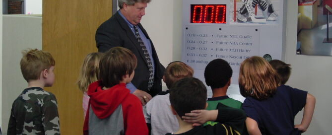 A group of students is guided in using a hockey exhibit by a man