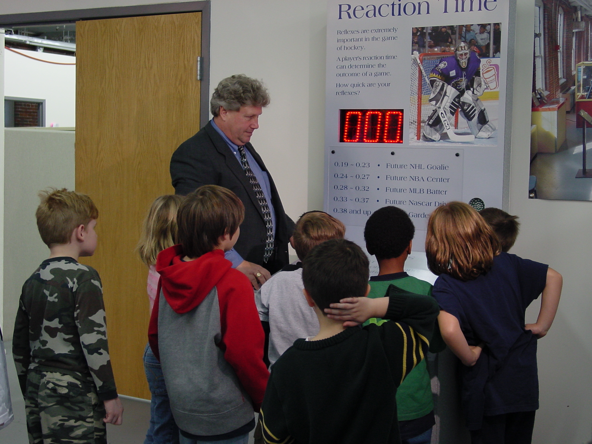 A group of students is guided in using a hockey exhibit by a man