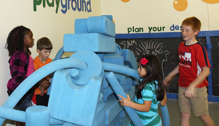 A group of children build a structure with large blue blocks and tubes