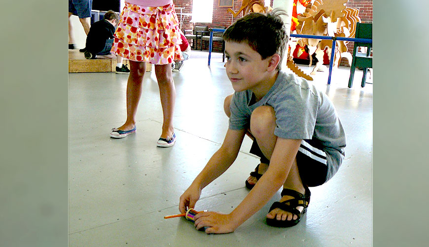 A boy bends down to the floor to start his wind up racer