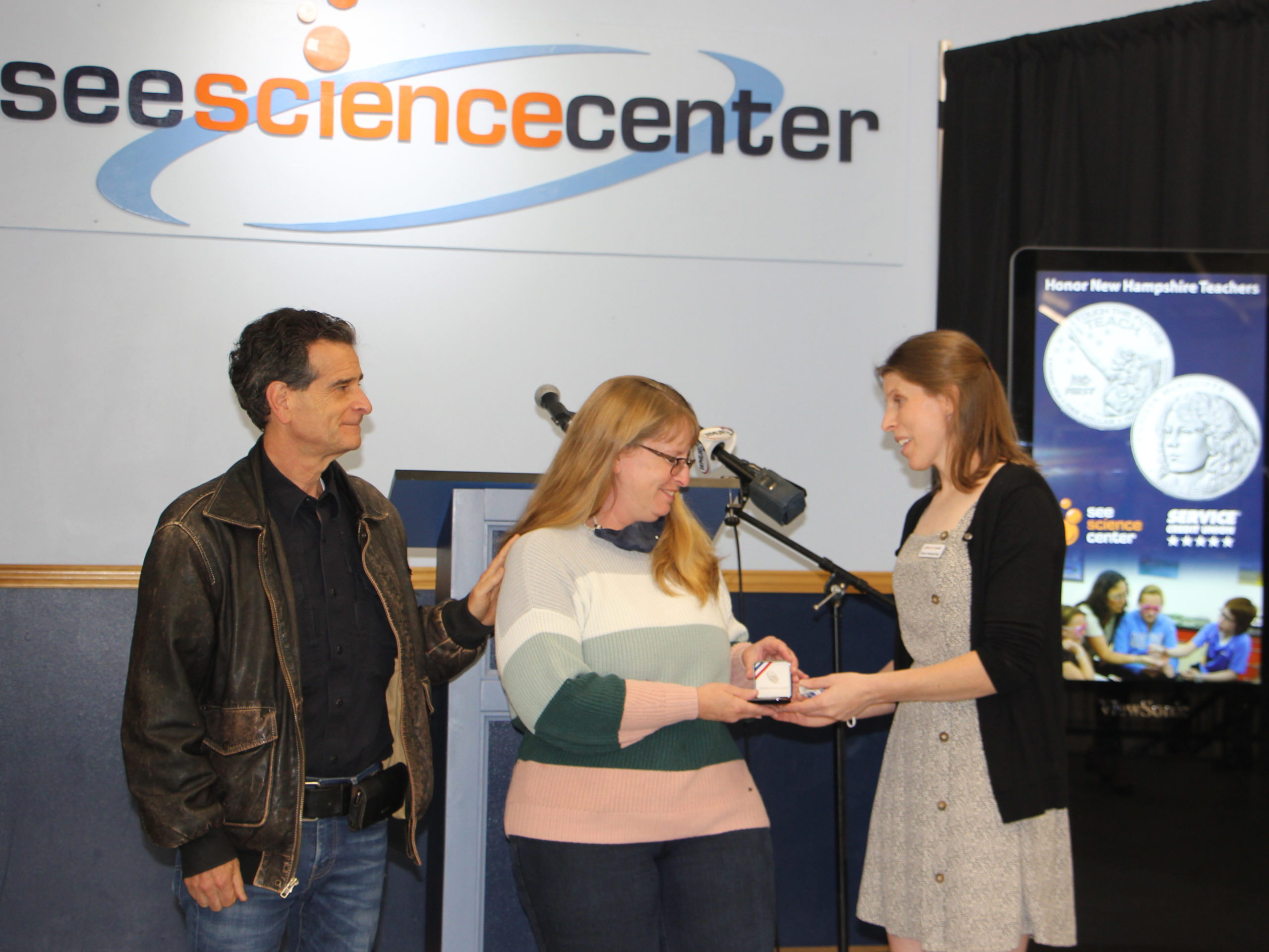 SEE Educator Becky Mayhew receives a coin from SEE director Shana Hawrylchak and Dean Kamen