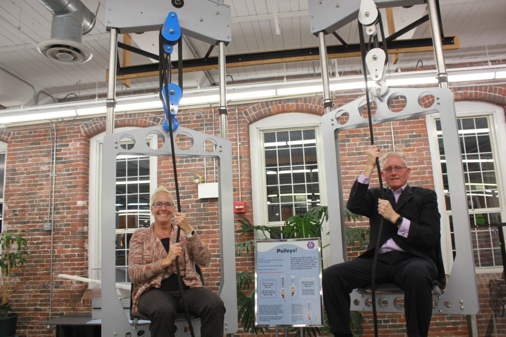 Two adults use the pulley chair exhibit at SEE.