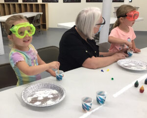 A young girl wearing safety goggles mixes a liquid in a cup.