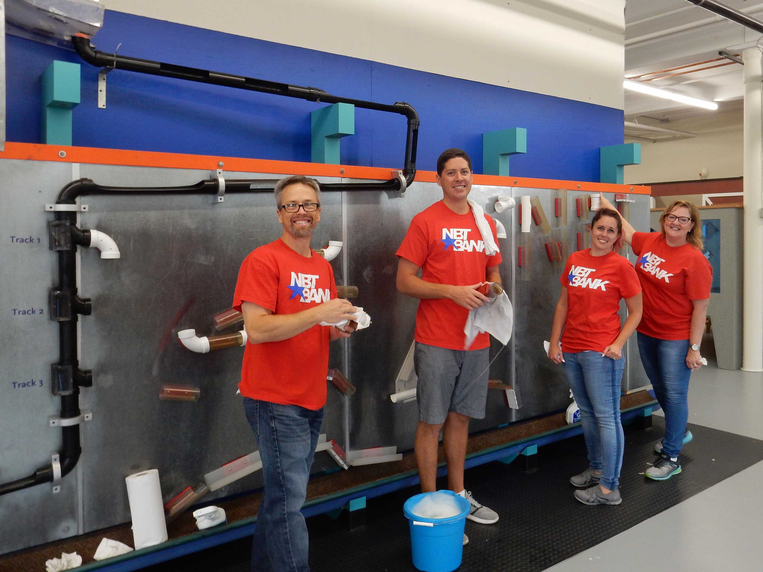 Four people with cleaning supplies stand in front of an exhibit.
