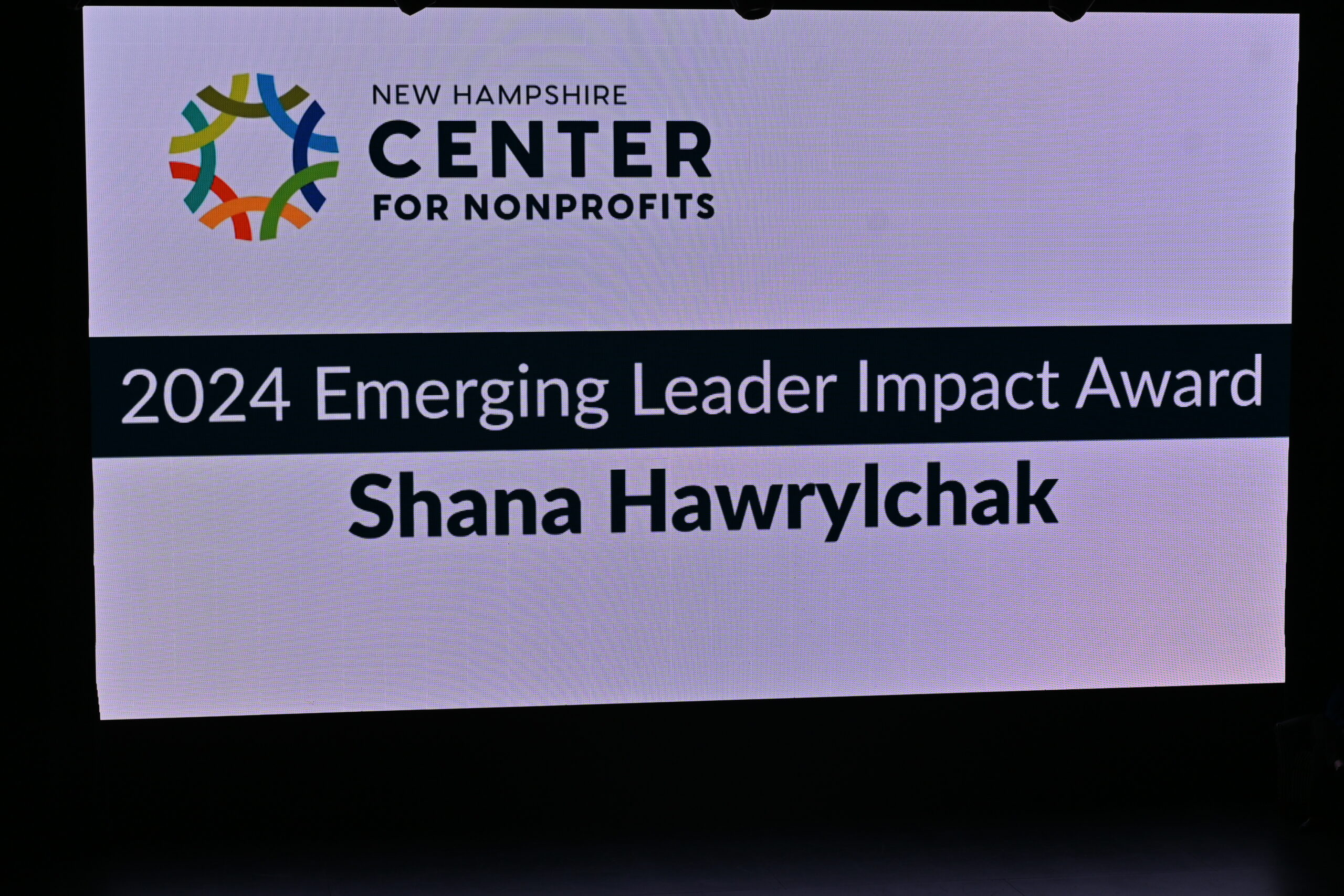 Screen on stage naming Shana HAwrylchak the 2024 Emerging Leader Impact Award Winner