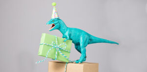 a dinosaur figurine wearing a party hat on a wrapped gift.