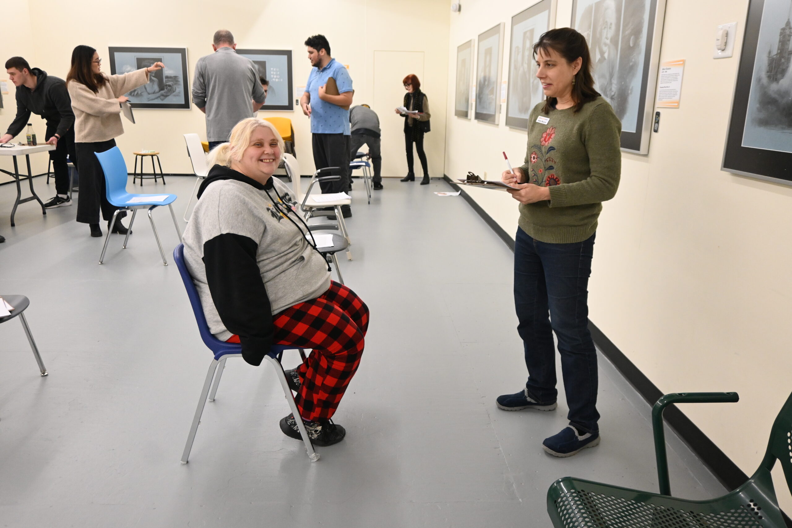 A woman seated in a chair gives feedback to a woman holding a clipboard.
