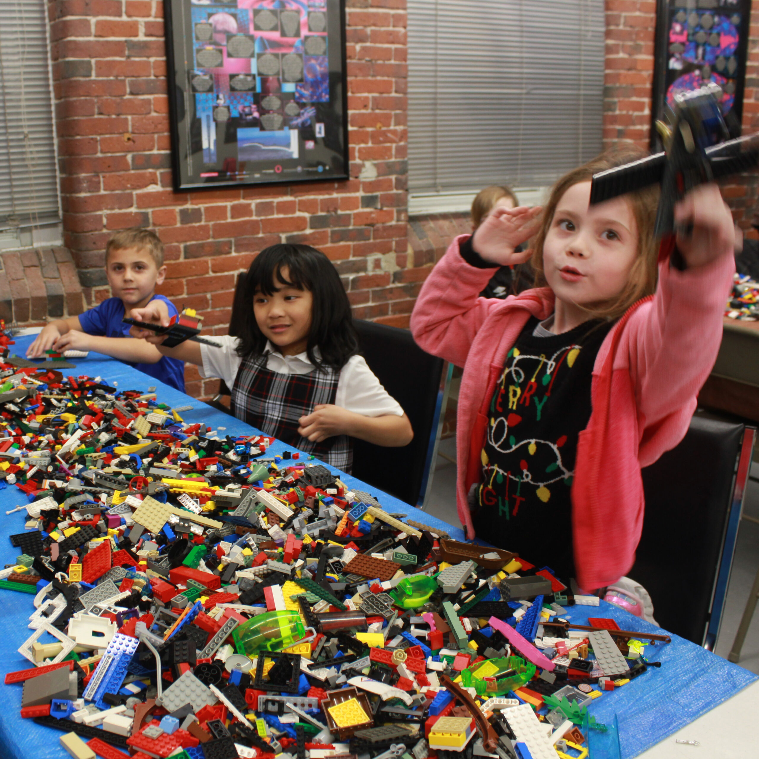 kids show off things they built with LEGO Bricks at a a table covered with LEGO Bricks.
