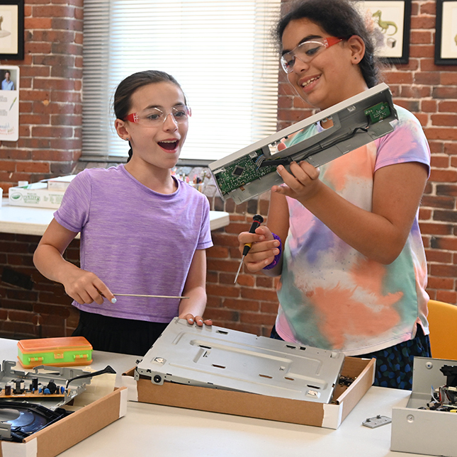 Two girls take apart a device to see what is inside.