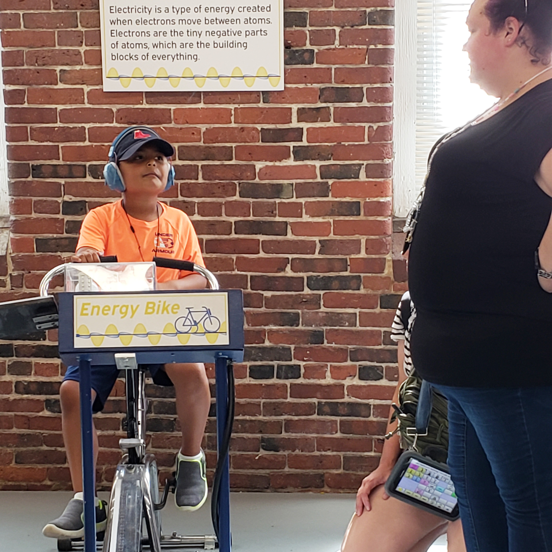A boy wearing noise cancelling headphones pedals the energy bike at SEE.