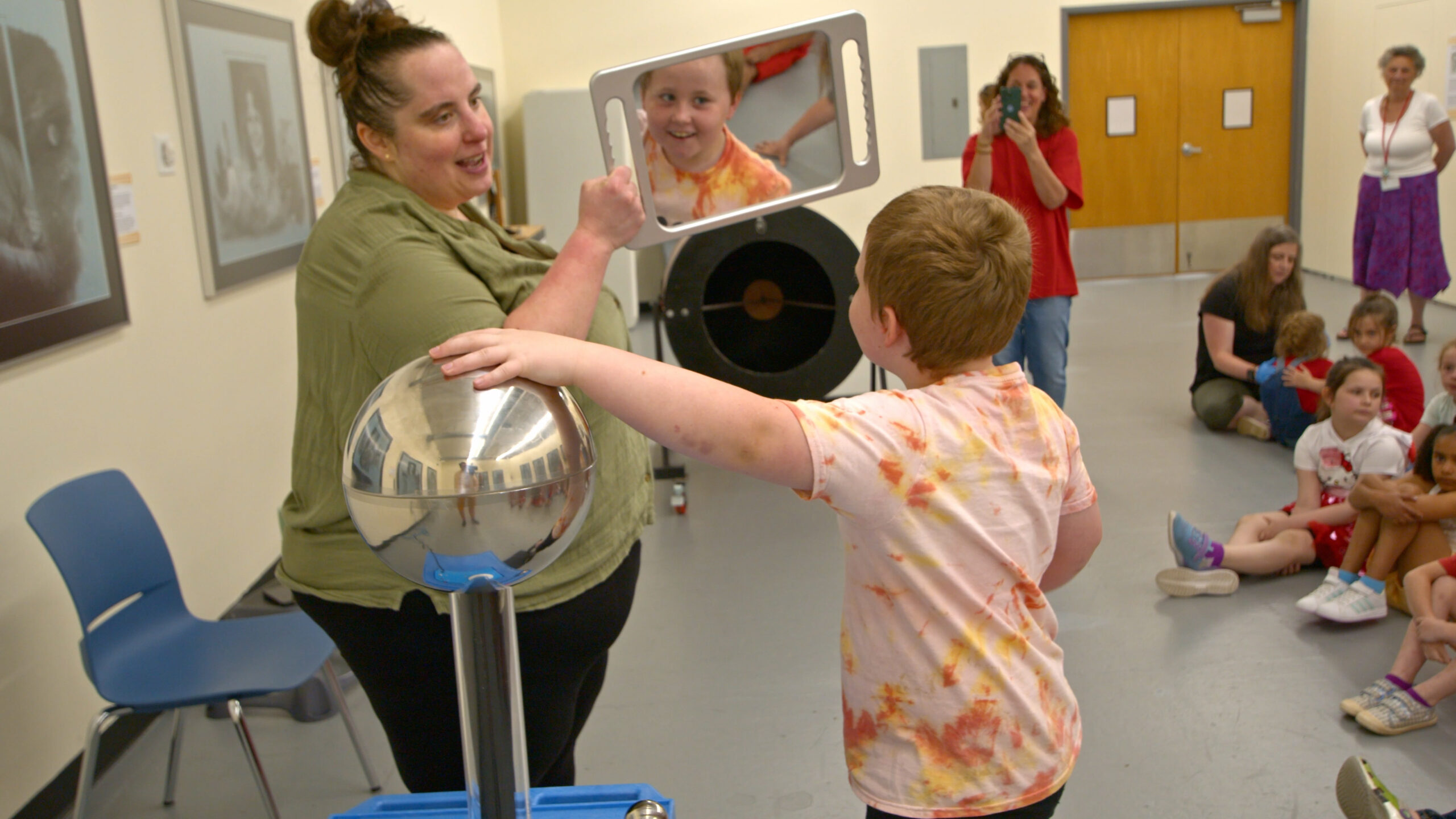 6.6 SEE02795574.00_00_42_09.Still002 A woman holds up a mirror to a boy with his hand on a van de graff generator with his hair sticking up.